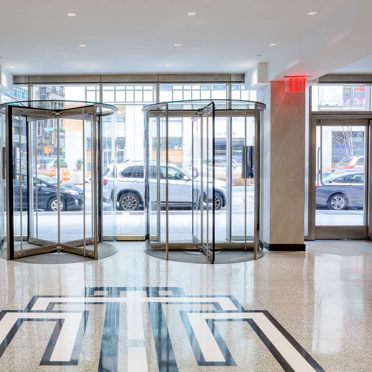A lobby area with revolving glass doors and a patterned floor, illuminated by natural light from large windows.