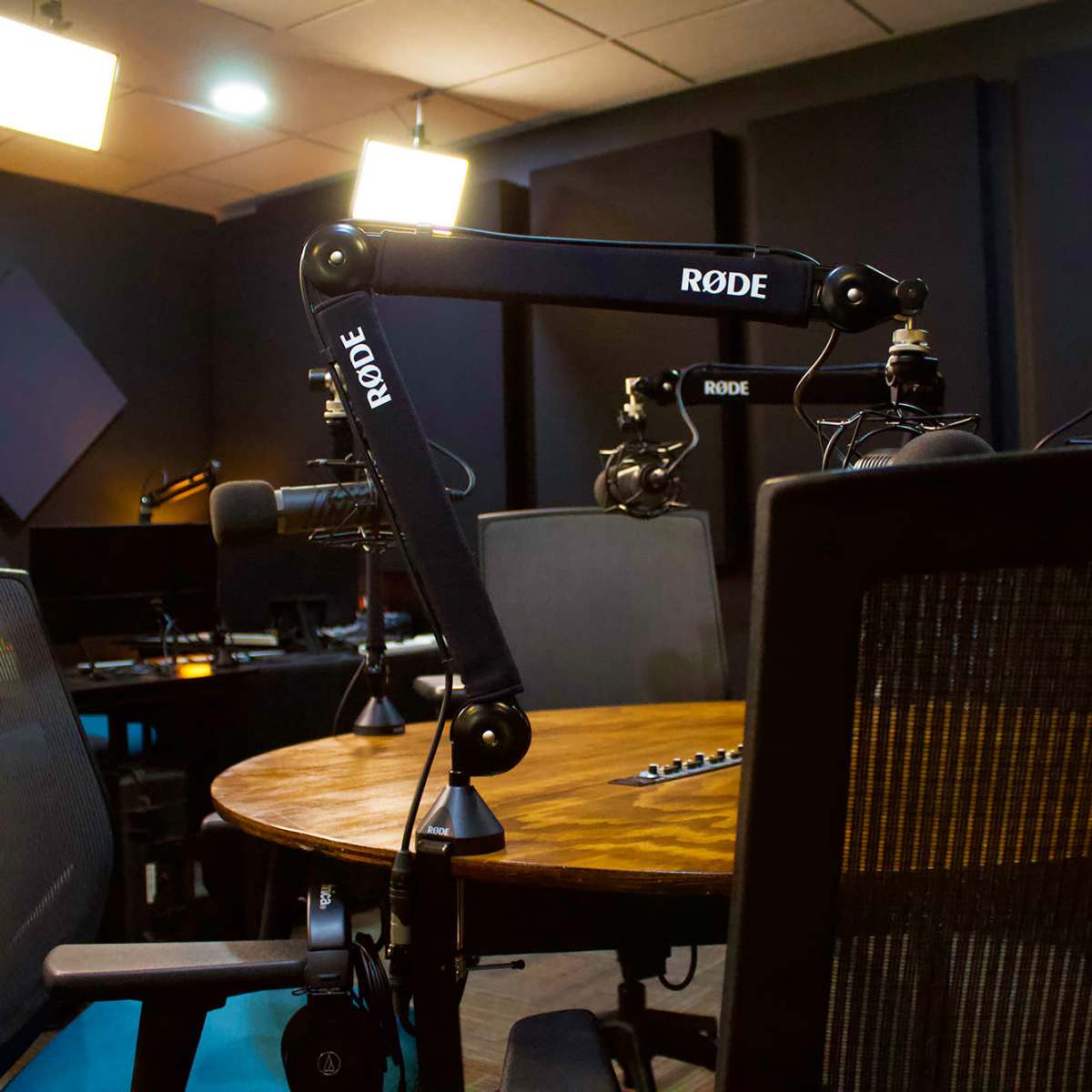 A podcast recording studio with microphones mounted on adjustable arms and a circular wooden table surrounded by black chairs.