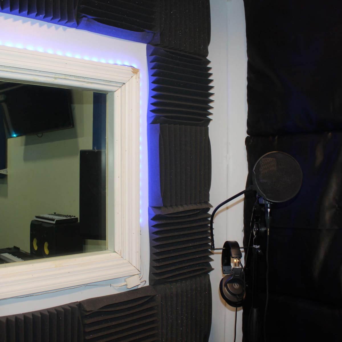 A recording studio booth with soundproofing panels, a microphone on a stand, and headphones hanging nearby.