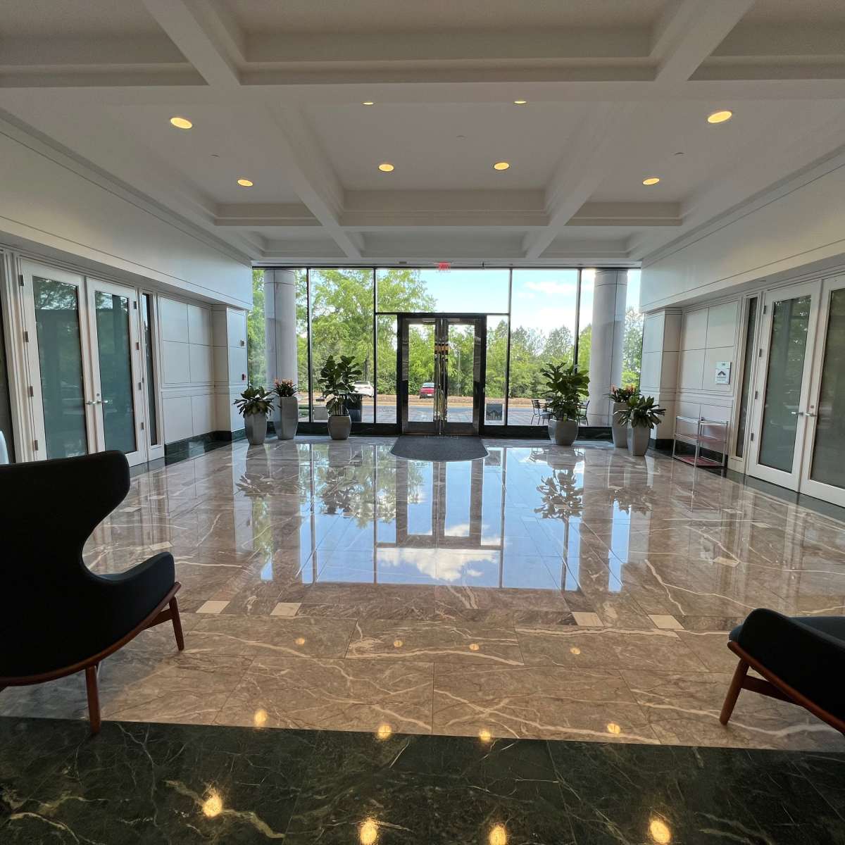 The lobby features marble flooring, large windows, and two modern chairs facing the entrance.
