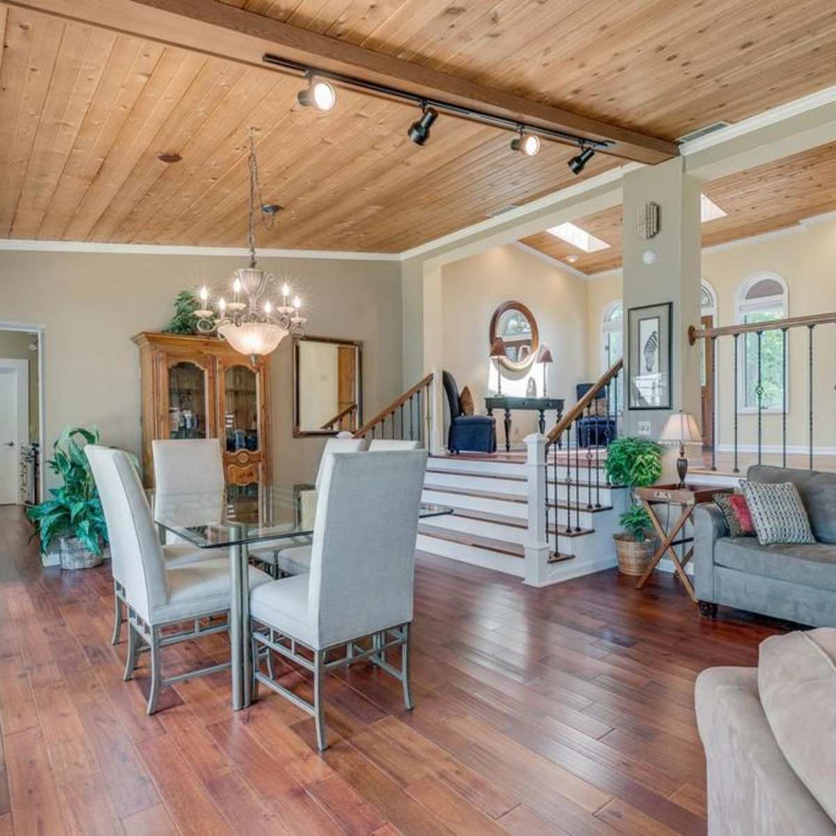 A spacious living area featuring a dining table, a comfortable sofa, wooden flooring, and a staircase leading to an upper level.