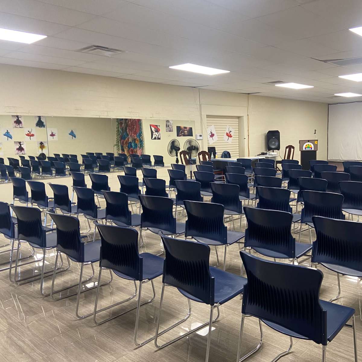 A classroom or meeting space filled with rows of blue chairs facing a blank projector screen.