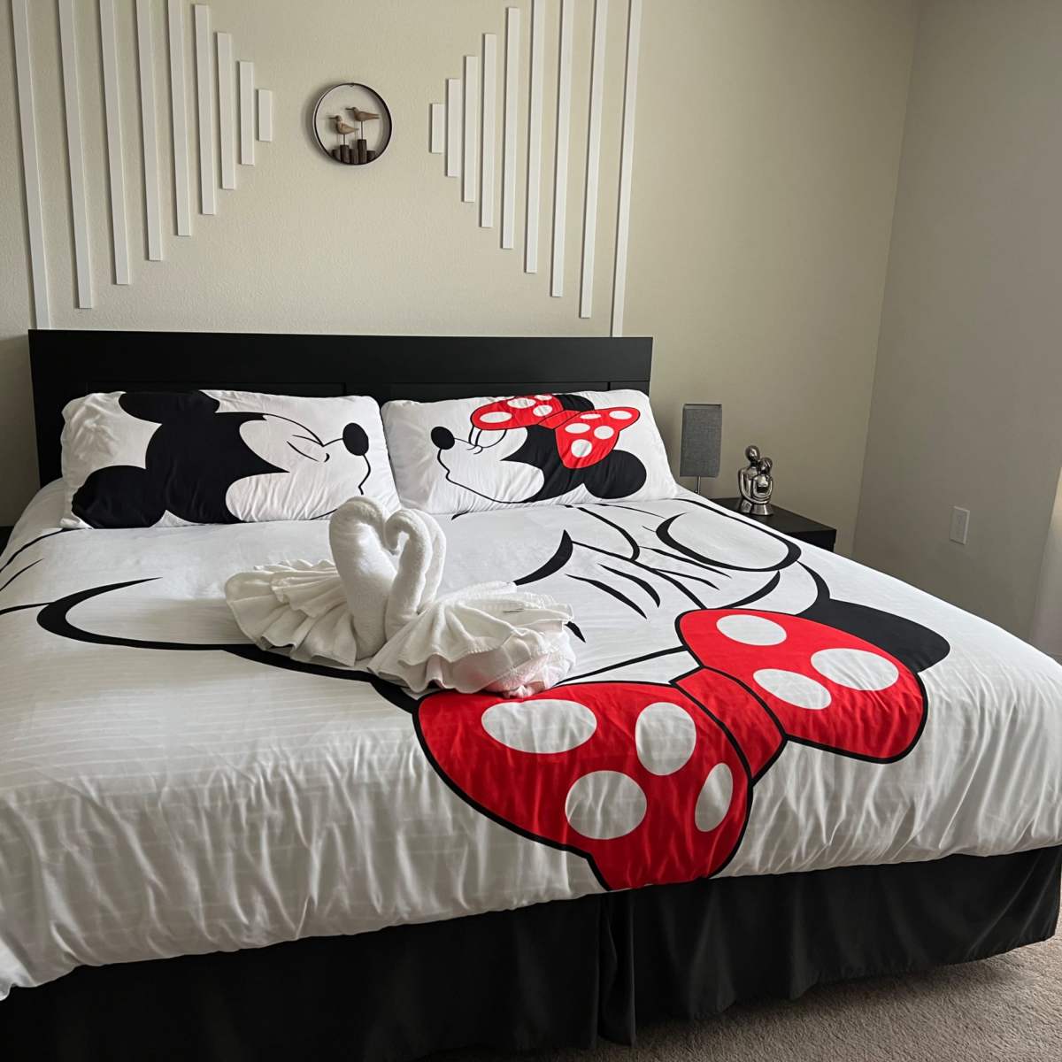 A bed with a Minnie Mouse-themed comforter features decorative towels shaped like a heart on top.