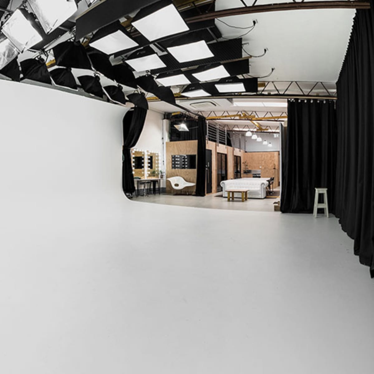 A spacious studio with a large white backdrop, overhead lights, and various furniture elements visible in the background.