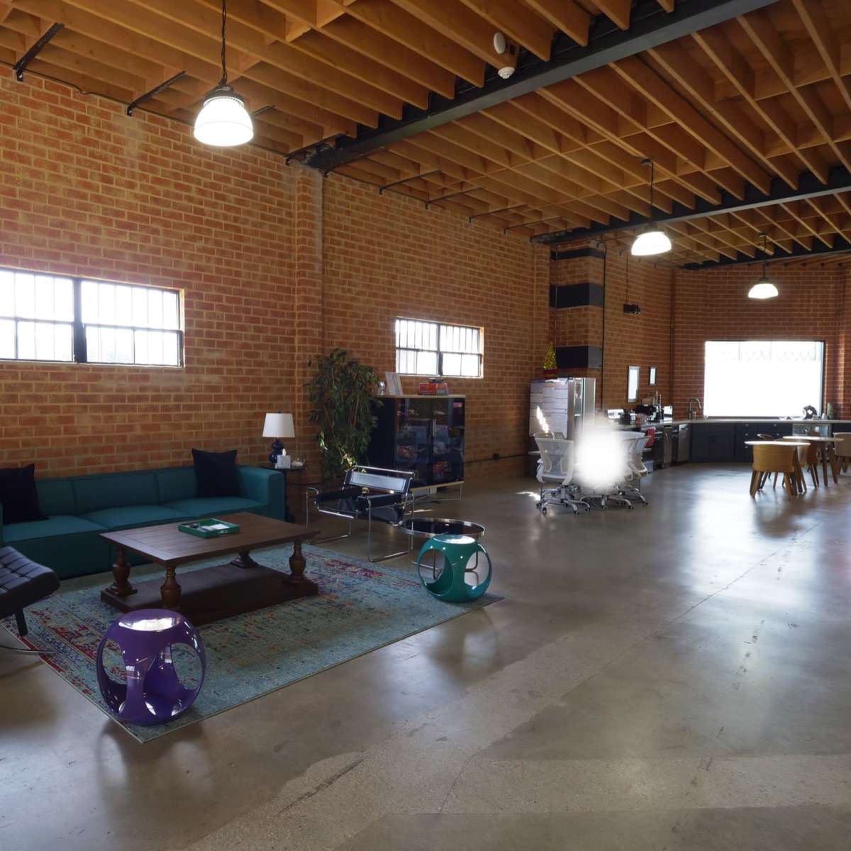 A spacious room features brick walls, a green couch, a coffee table, and a kitchen area in the background.
