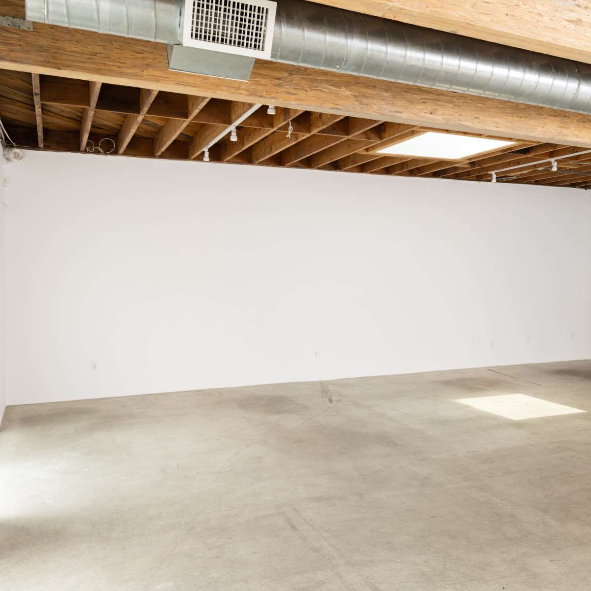 An empty room with a concrete floor, exposed wooden beams, and a large blank wall.