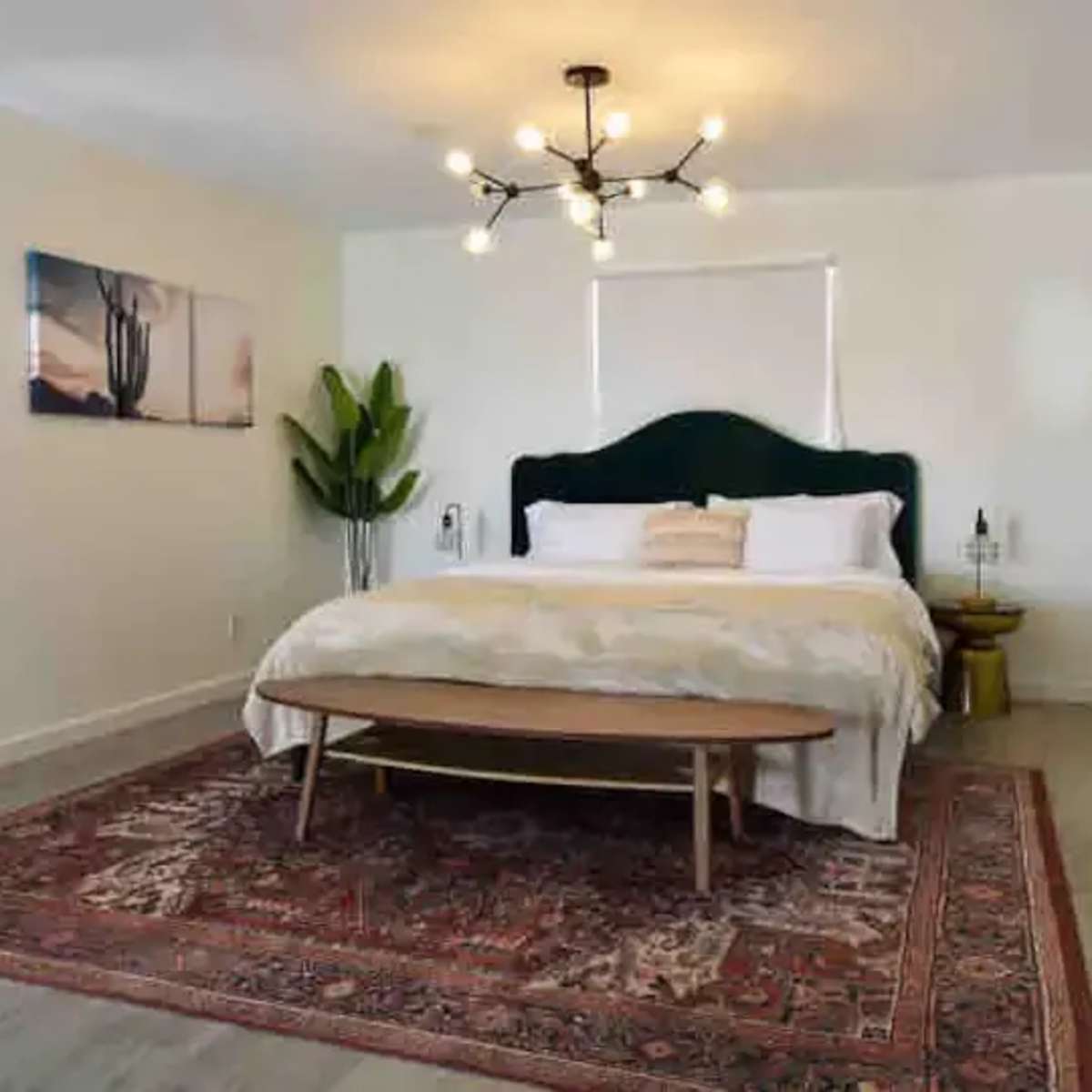 A modern, well-lit bedroom with a large bed, a wooden table in front, and decorative plants.