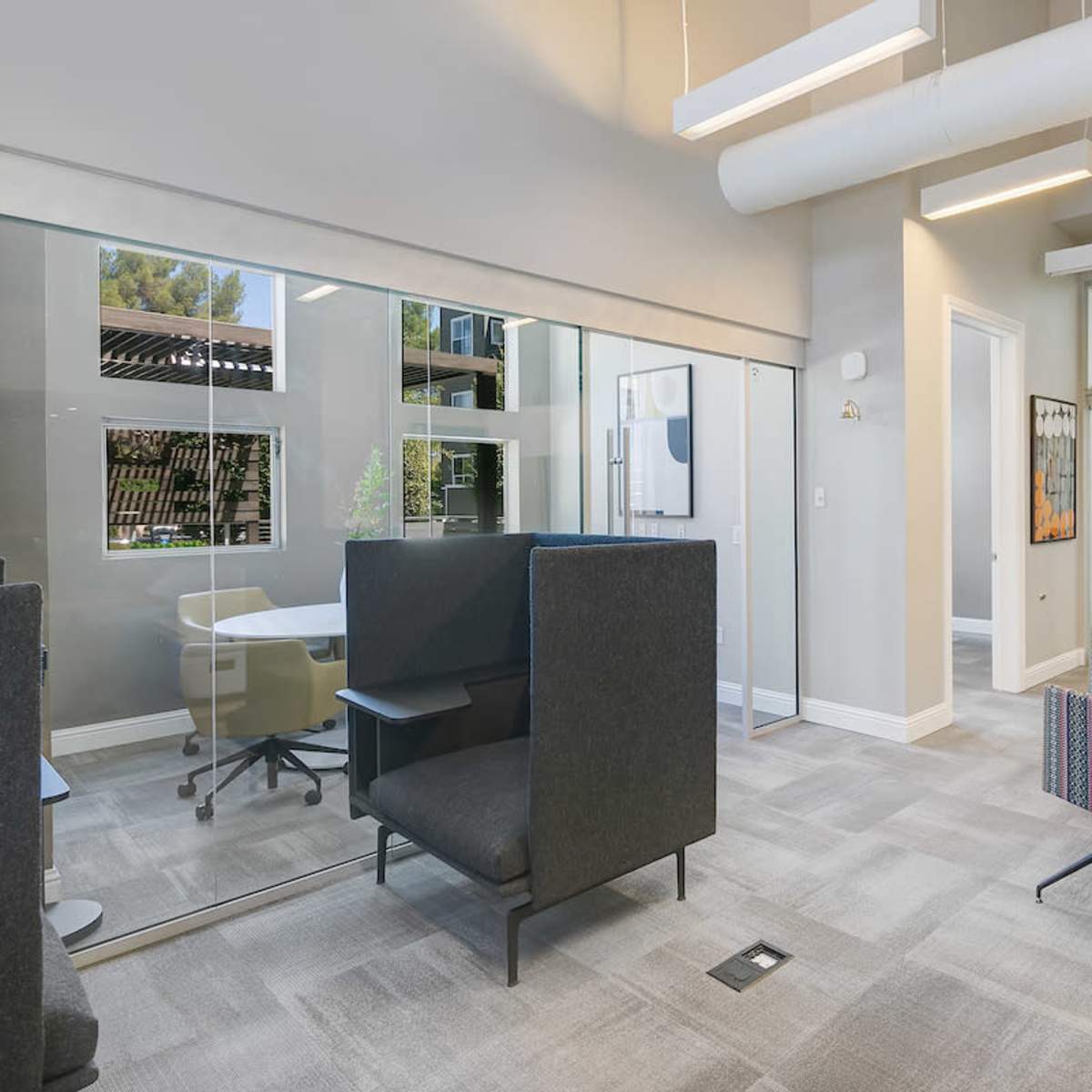 A modern office space featuring a seating area with a couch and chairs, glass partitions, and a meeting room.