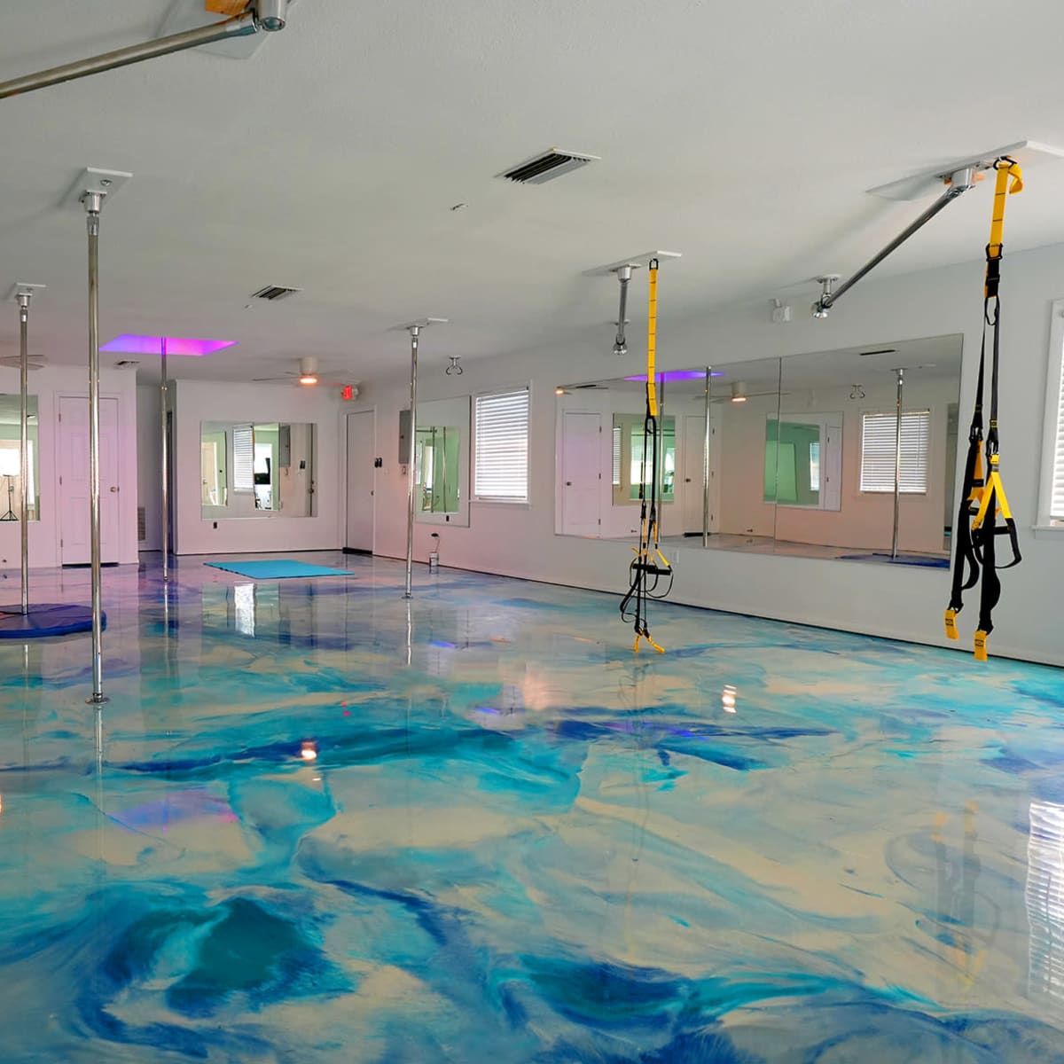 A spacious room with a glossy, blue-and-white marbled floor, equipped with mirrors and suspension training equipment hanging from the ceiling.