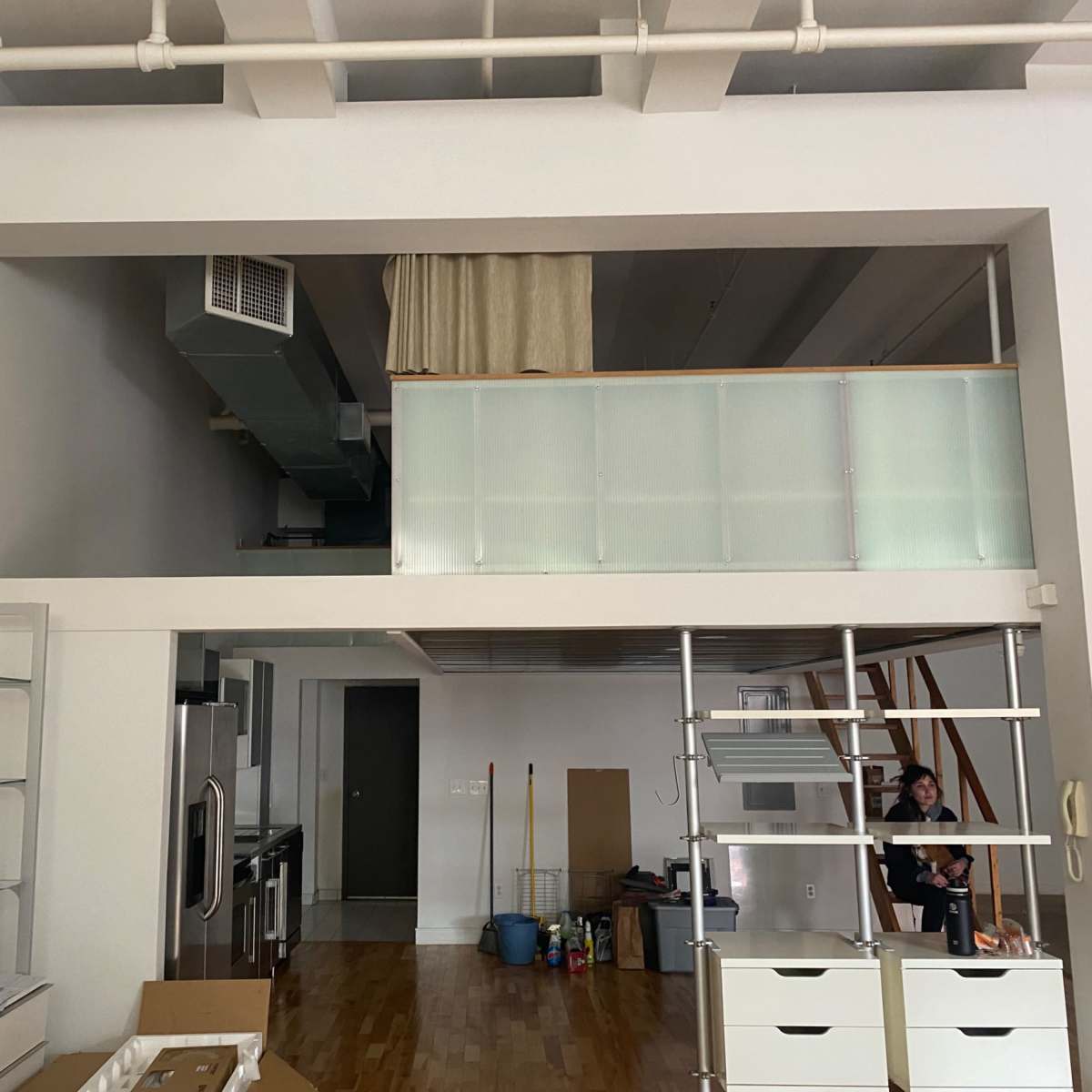 A spacious, unfinished interior of a loft-style apartment with a kitchen area and a raised platform featuring a railing.