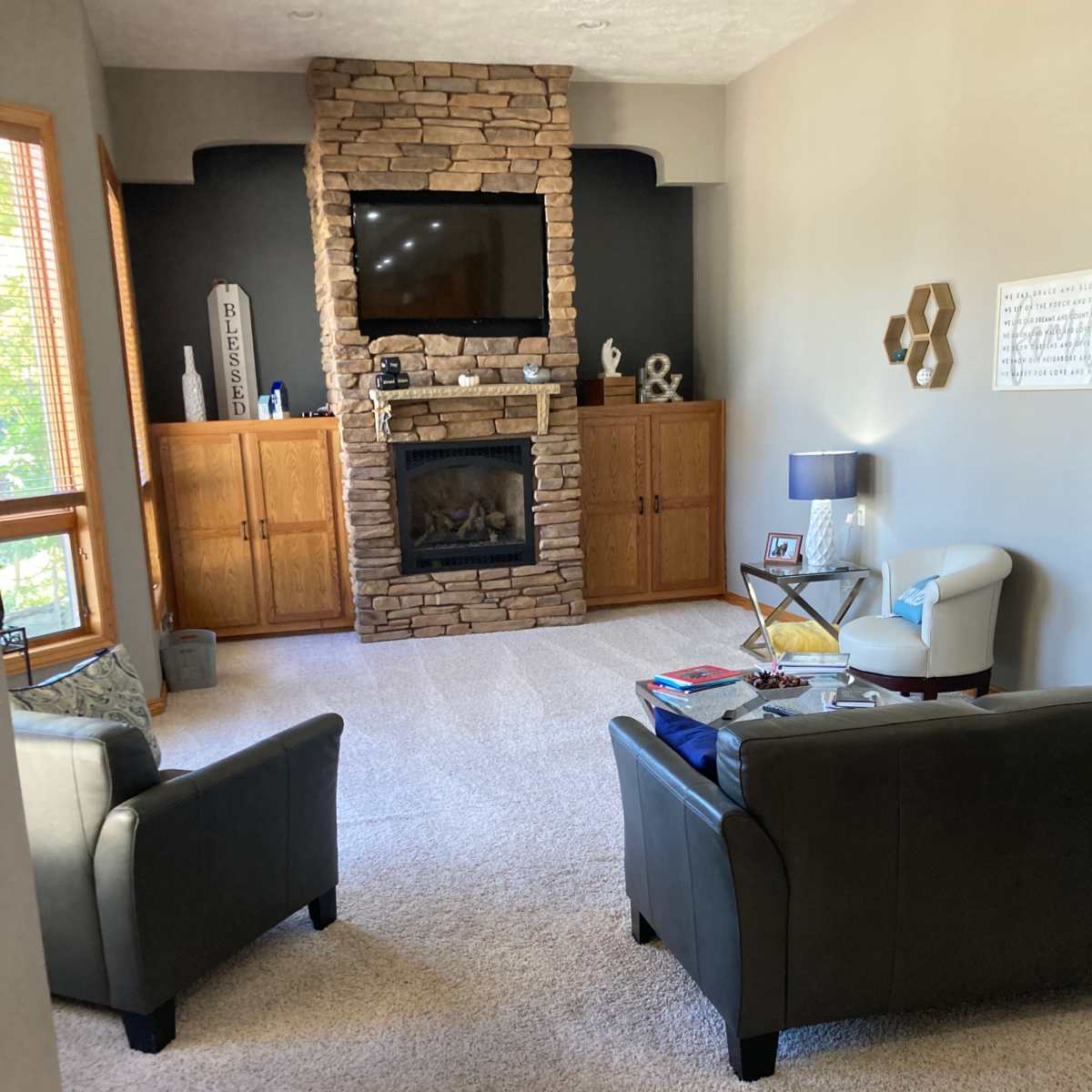 A living room with two chairs facing a stone fireplace and a mounted television, surrounded by wooden cabinets and decorative items.