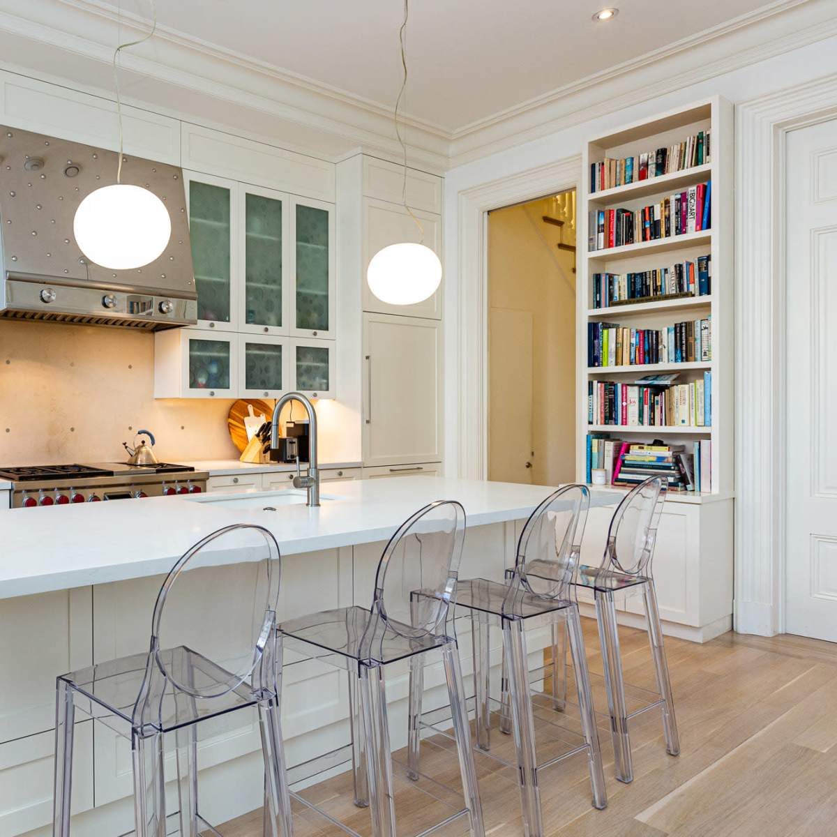 A modern kitchen with white cabinetry, a large island with transparent stools, and overhead pendant lights.