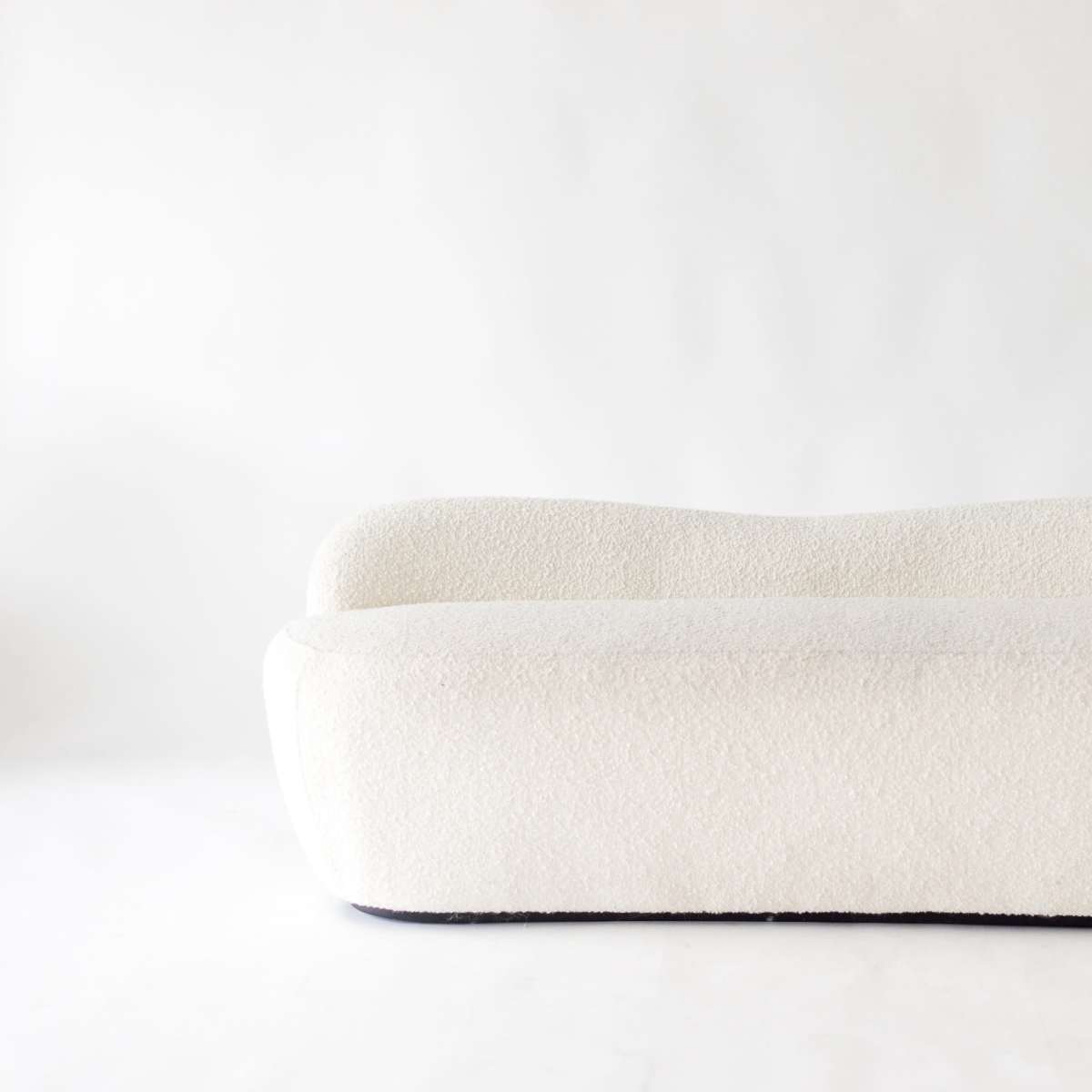 A white, rounded sofa with a textured fabric sits against a plain background.