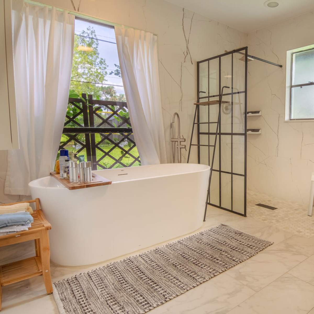 A modern bathroom featuring a freestanding bathtub, a glass-enclosed shower, a toilet, and large windows allowing natural light to enter.
