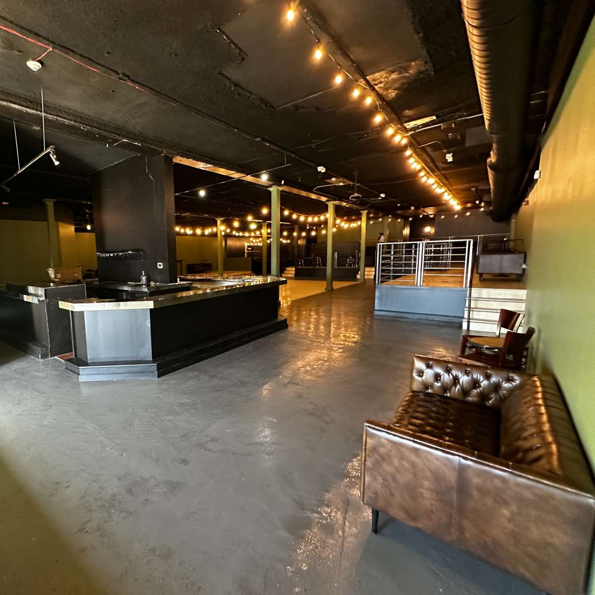 A spacious, dimly lit interior of a commercial establishment with exposed ceiling beams, polished concrete floors, and a bar counter on one side.