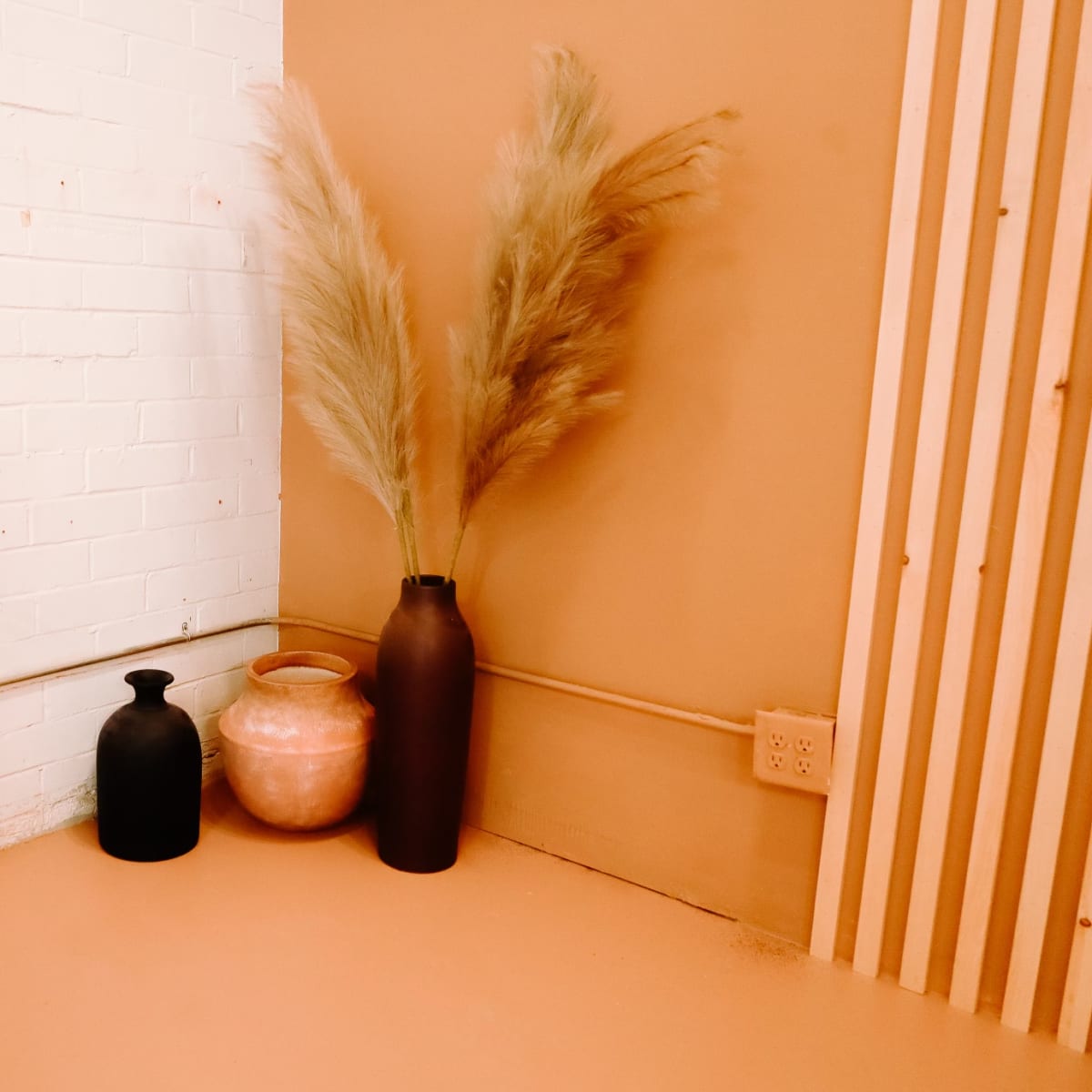 A corner of a room with a clothing rack on the left, featuring wooden hangers, and three decorative vases in neutral colors against a tan wall.