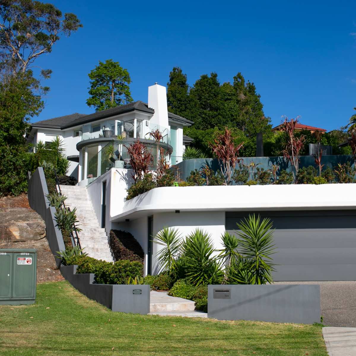 A modern two-story house with a curved roof, a large garage, and landscaped gardens.