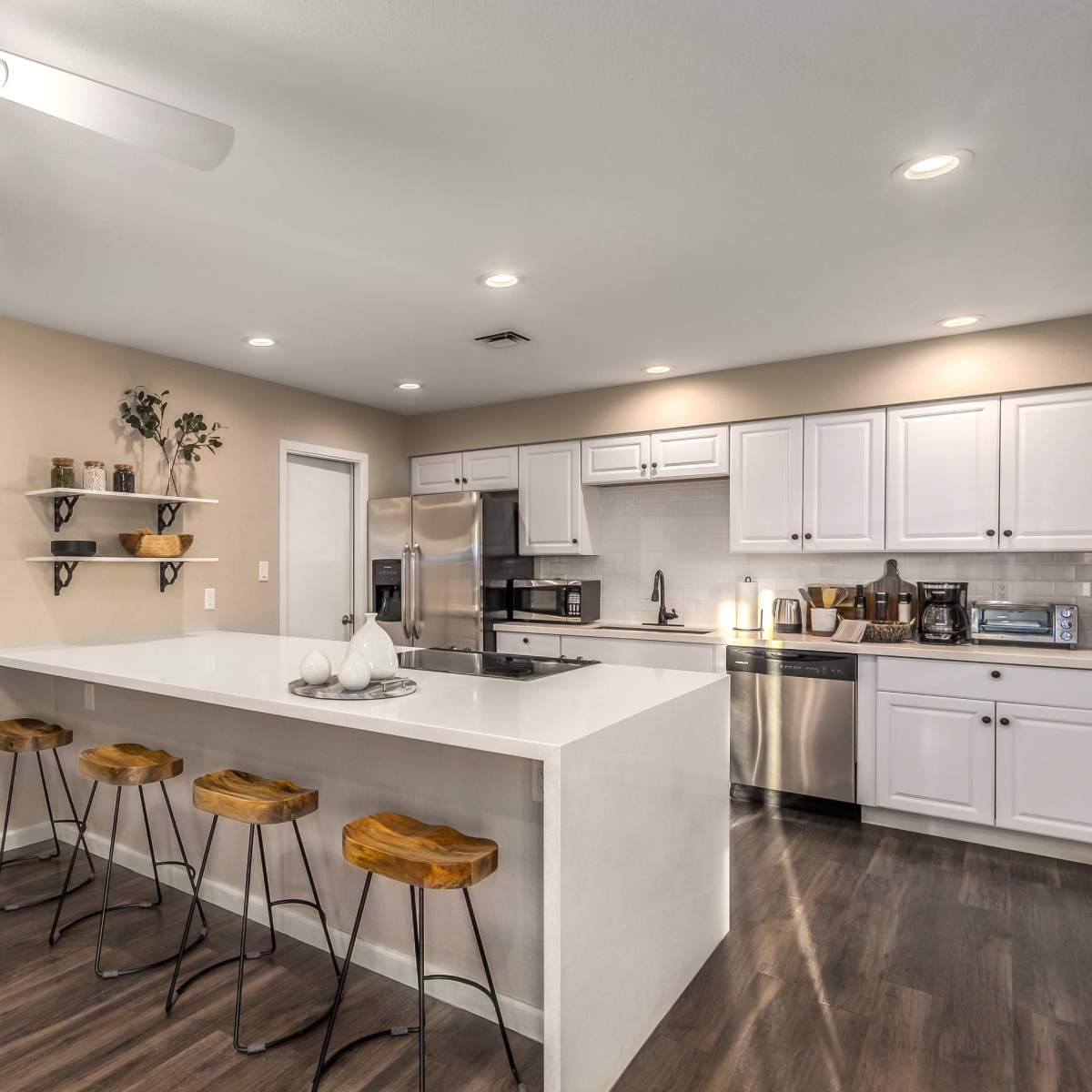 A modern kitchen features white cabinetry, stainless steel appliances, and a large island with bar stools.