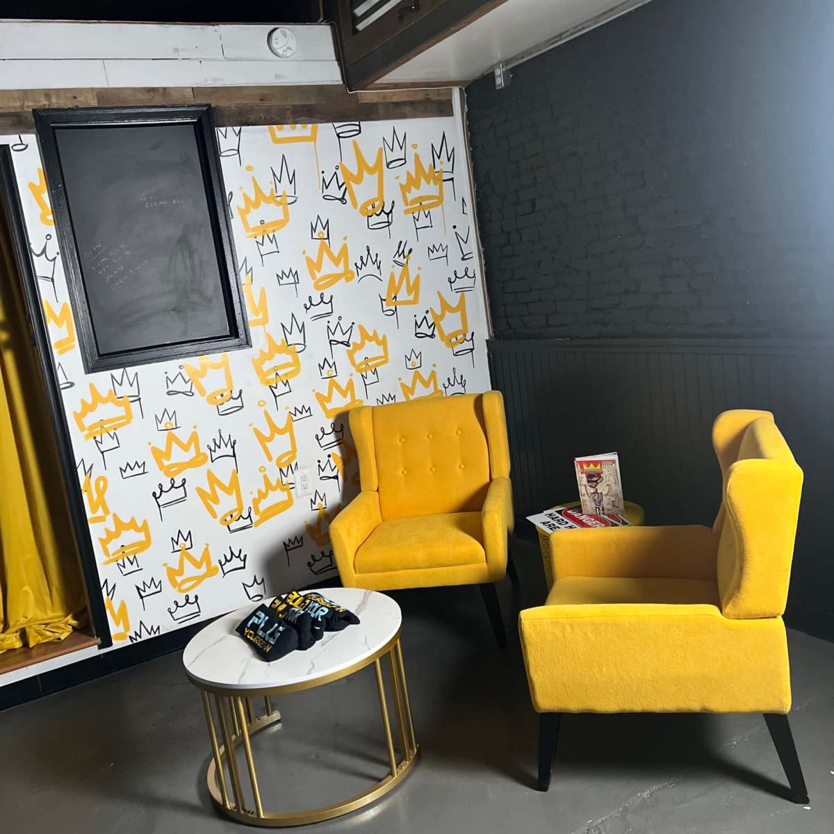 The scene features two yellow chairs and a round coffee table on a gray floor, set against a wall with a white and yellow crown-patterned design.