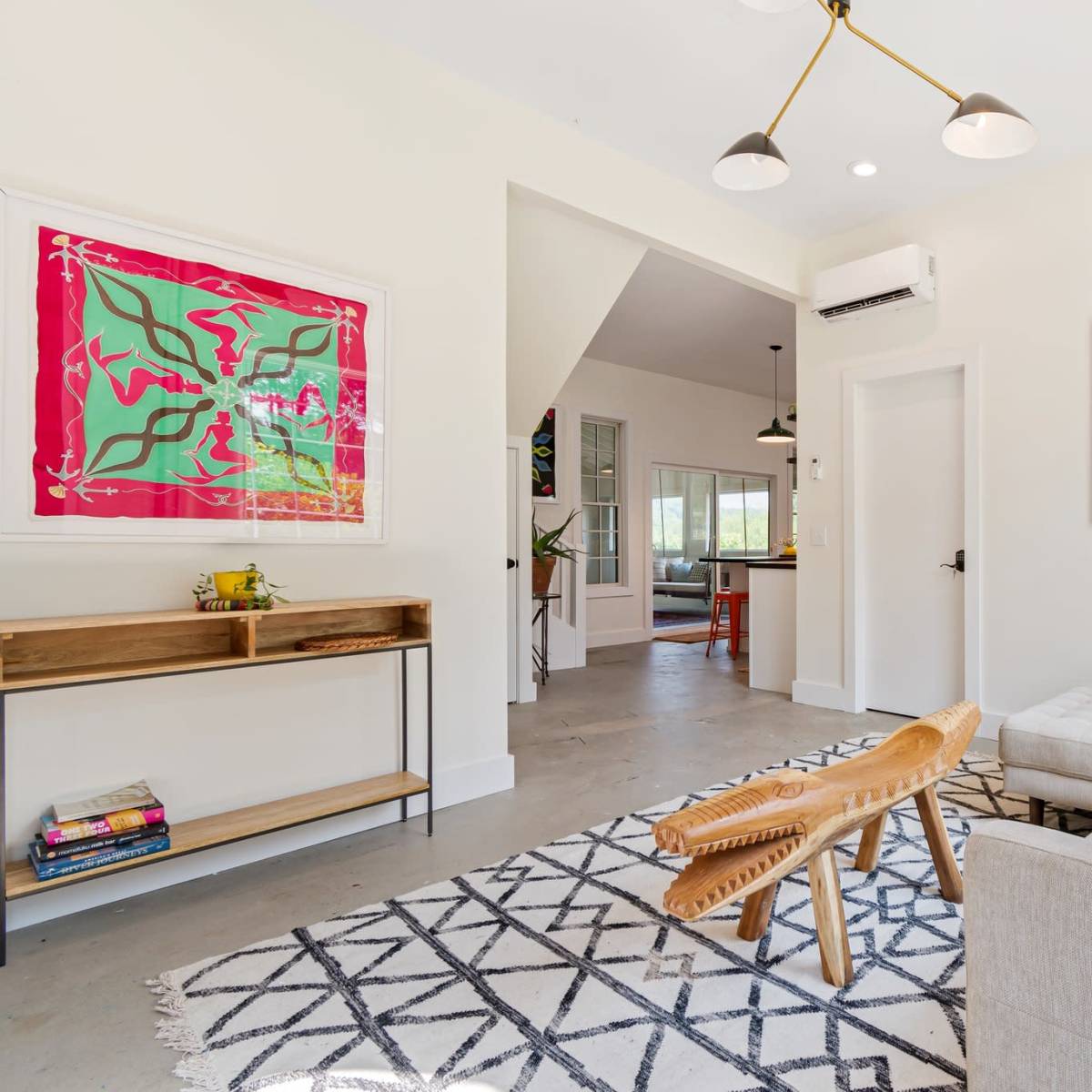 A modern living room with a light-colored sofa, a wooden bench, and colorful wall art, featuring a patterned rug on the floor.