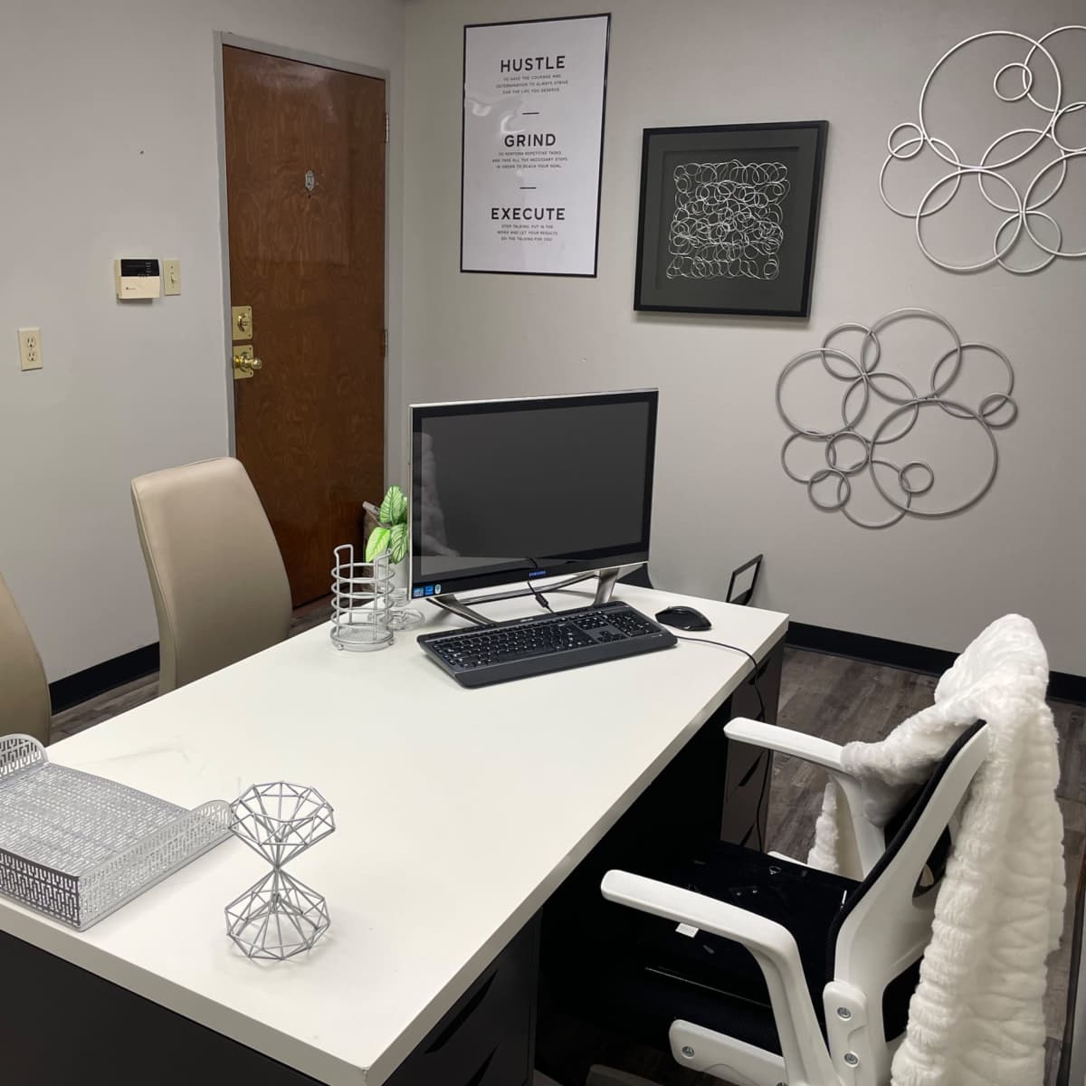 A small office with a desk, a computer, two chairs, and wall decorations.