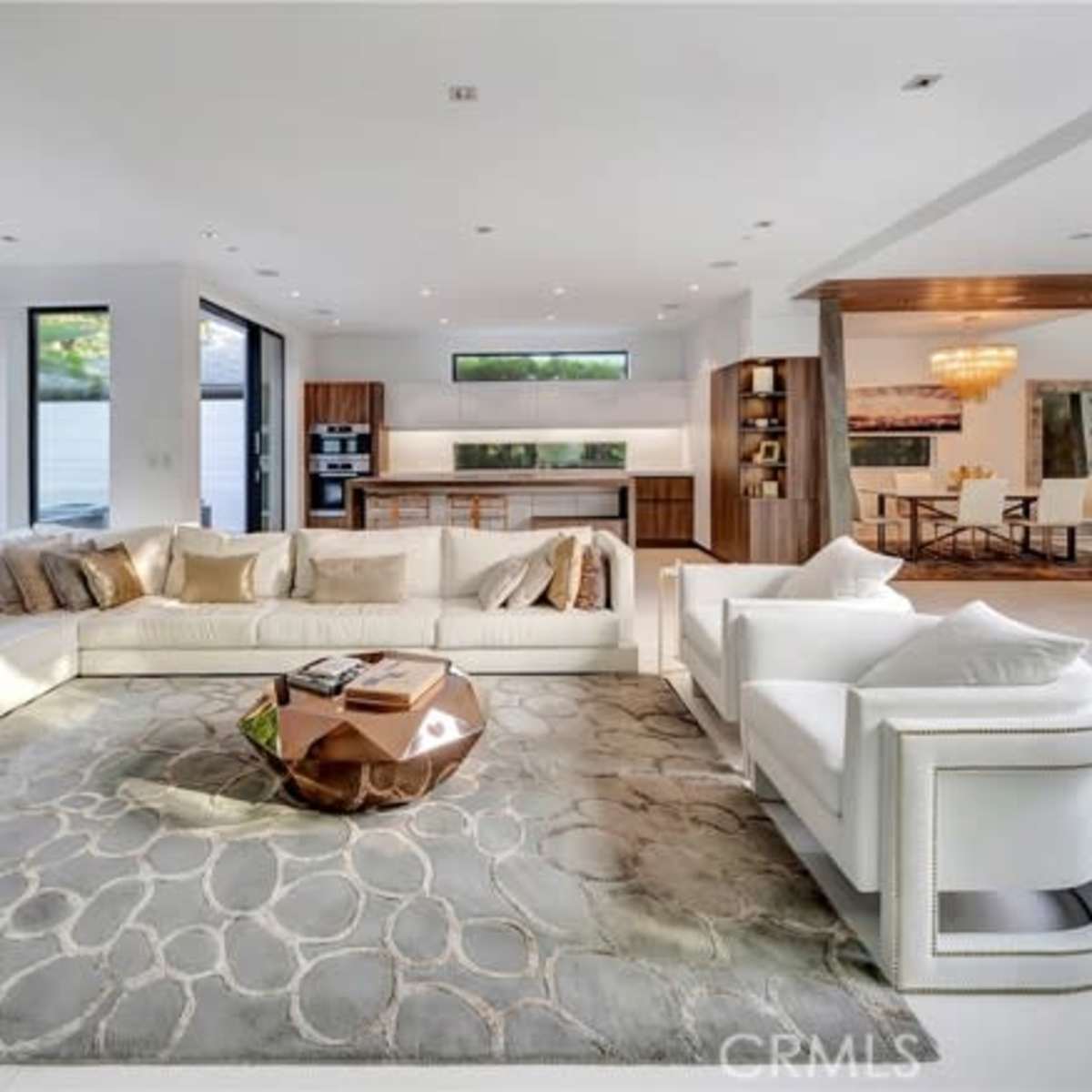 The living room features a large white sectional sofa, a decorative coffee table, and floor-to-ceiling windows overlooking a lush outdoor space.