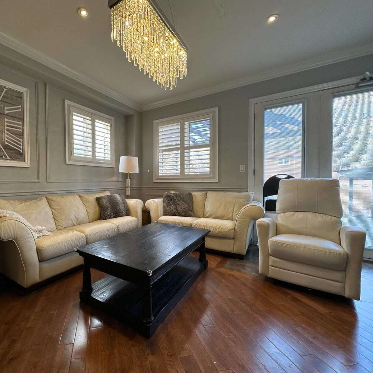 The living room features a white leather sofa set arranged around a dark wooden coffee table, accented by a chandelier and large wall clock.