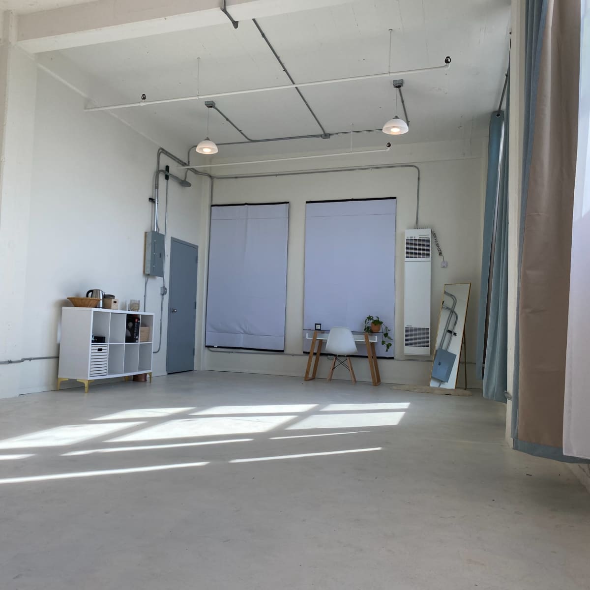 A spacious, empty room with white walls, large windows, and minimalist furniture, including a chair and a small shelf.