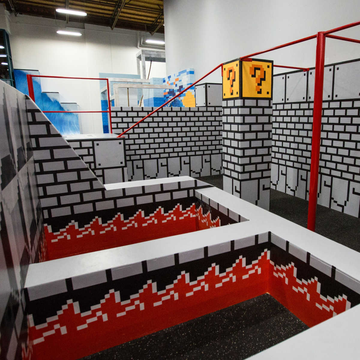 A colorful indoor obstacle course designed to resemble a video game level, featuring brick walls, question mark blocks, and a multi-level layout with red accents.