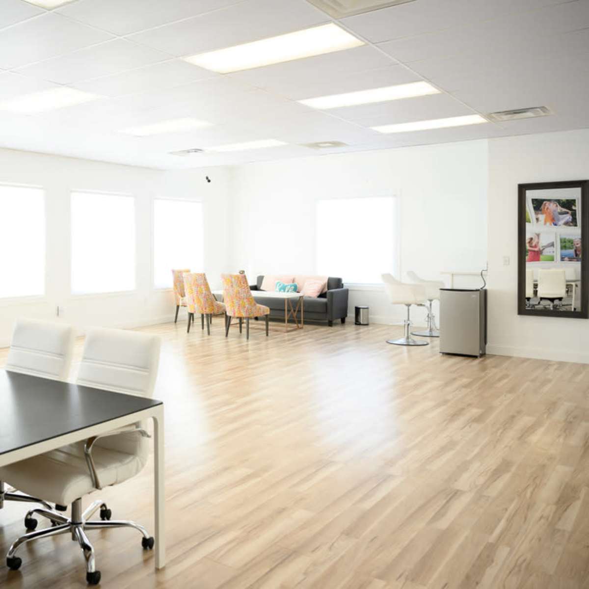 A bright and open office space features a large conference table with white chairs on one side and a lounge area with colorful seating on the other side.