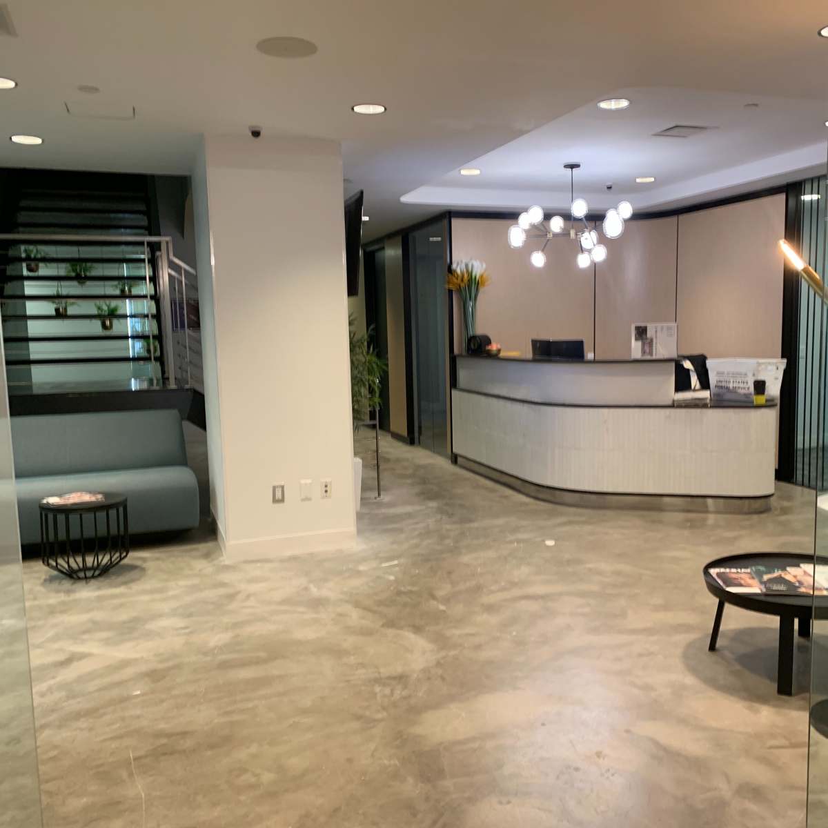 A modern reception area with a front desk, seating, and a staircase in a well-lit space surrounded by glass panels.