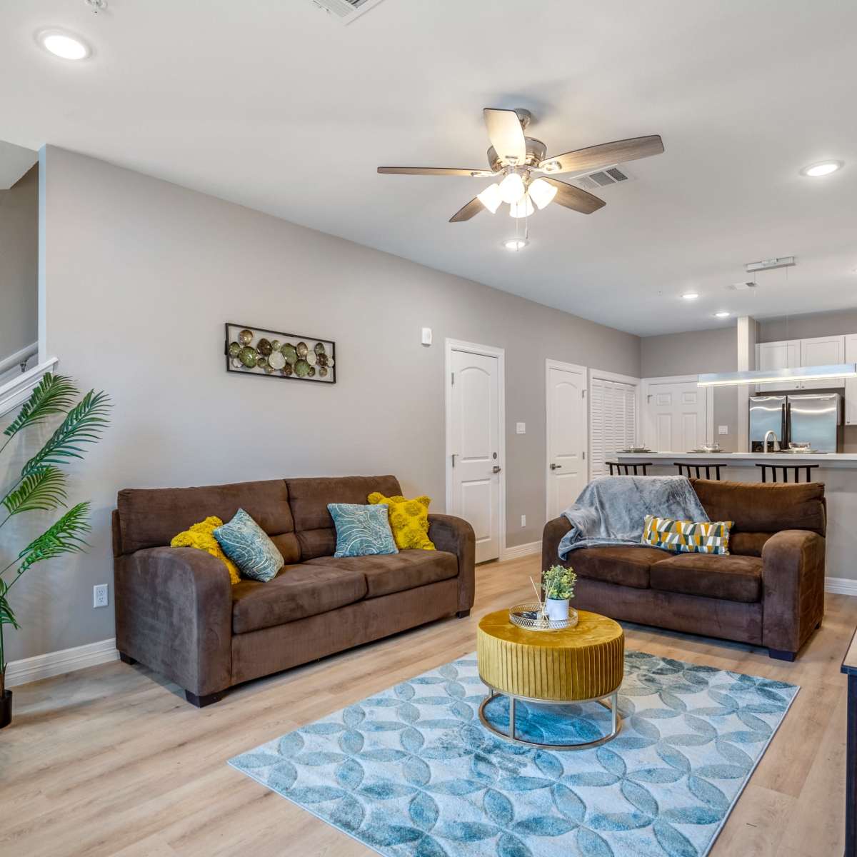 A modern living room with two brown sofas, a yellow coffee table, and a staircase leading to an upper level.