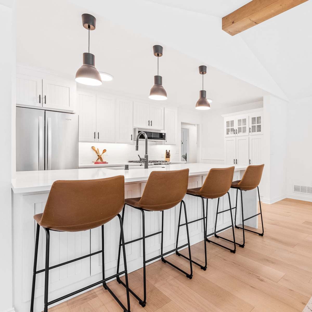 A modern kitchen features a white island with four brown bar stools and pendant lighting above.