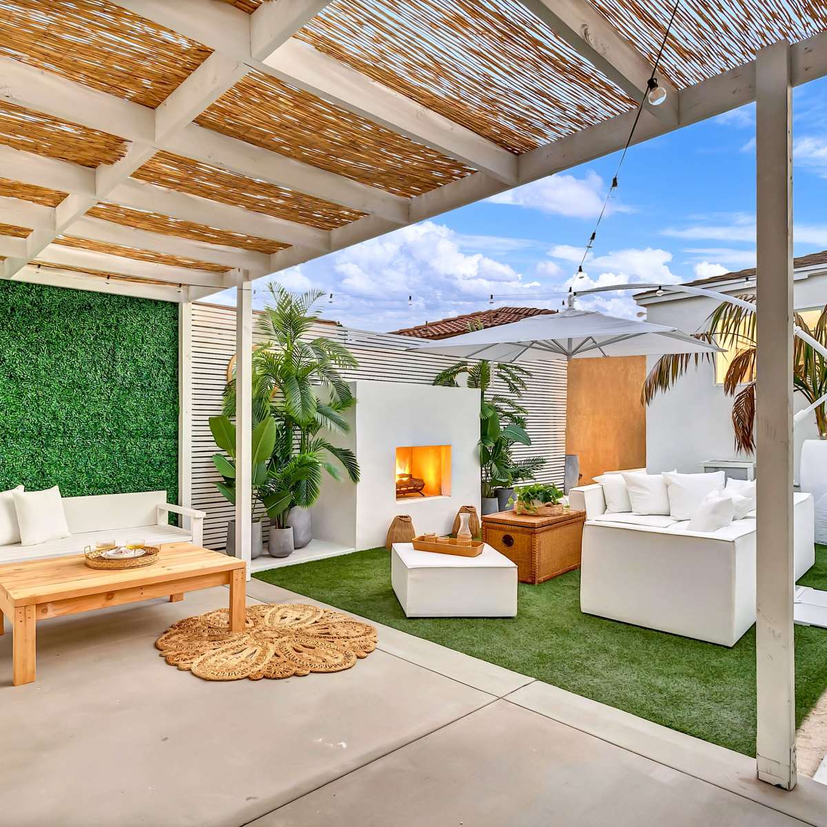 A modern outdoor living space with a seating area, a fire pit, greenery, and a covered patio.