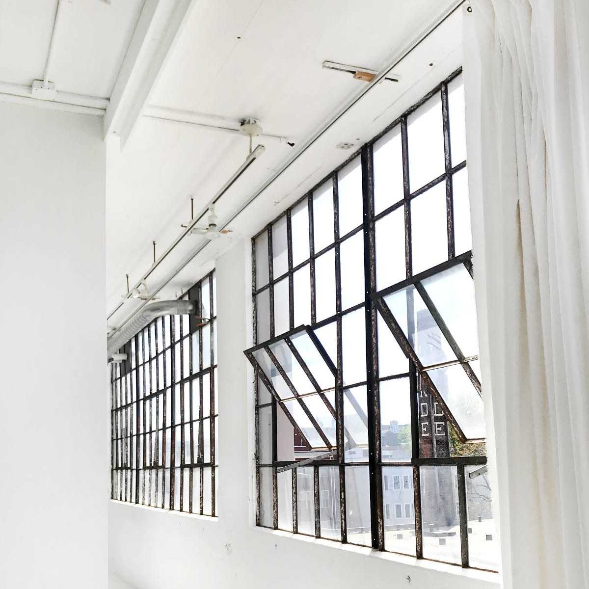 A bright, minimalist room with large industrial windows and sheer curtains.