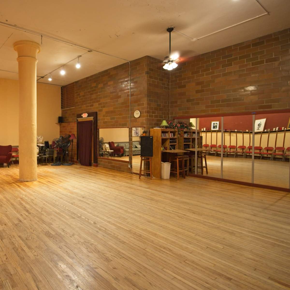 A spacious dance studio with wooden floors, a mirrored wall, and seating along one side.