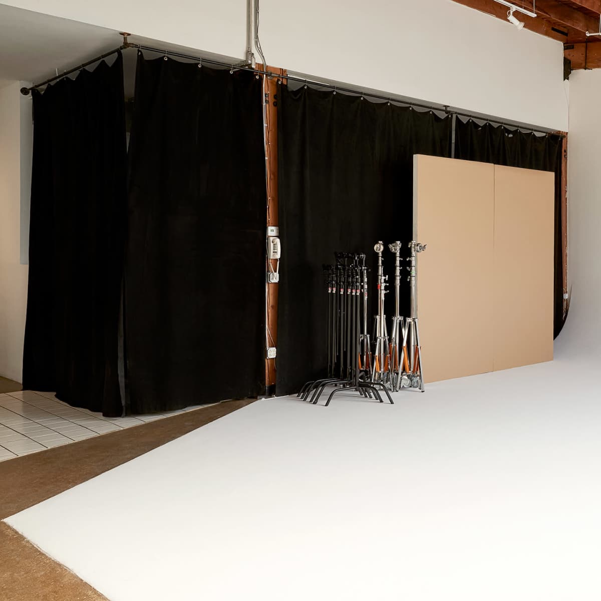 A photography studio featuring a white backdrop, black curtains, and several light stands on a support rack.