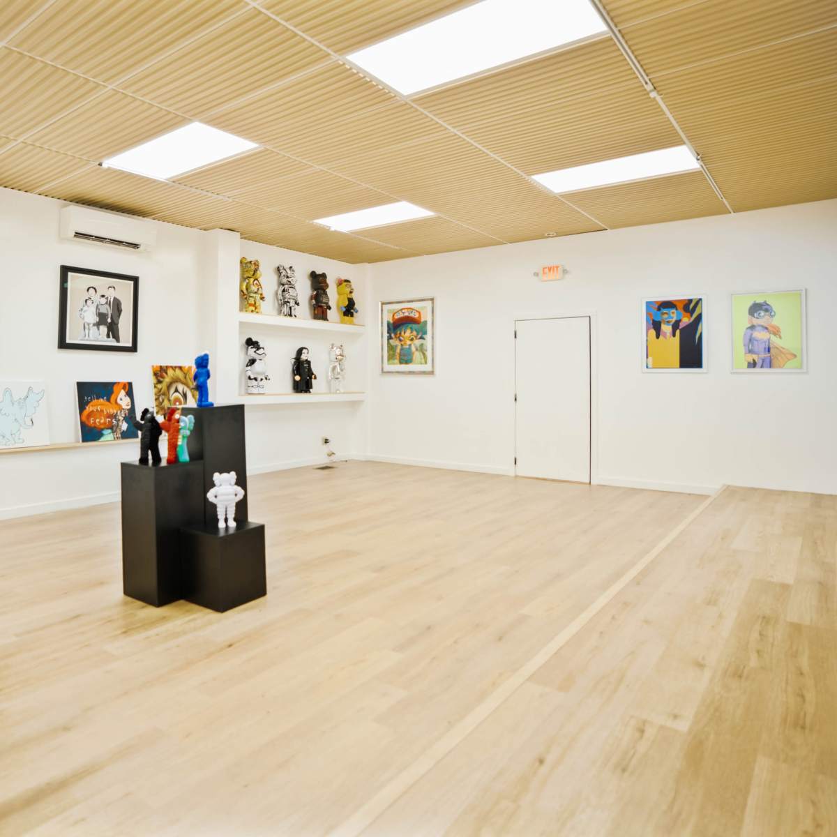 An empty art gallery with wooden flooring, white walls featuring various artworks, and a central display stand.