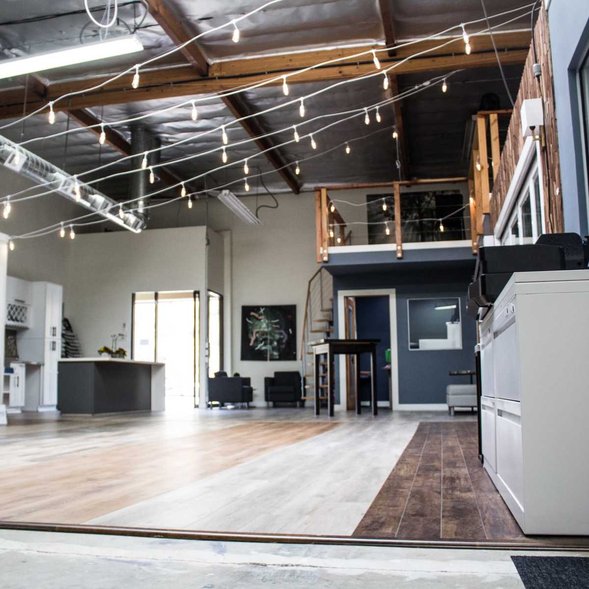 A spacious, modern office interior with wooden flooring, industrial lighting, and a second-level loft area.
