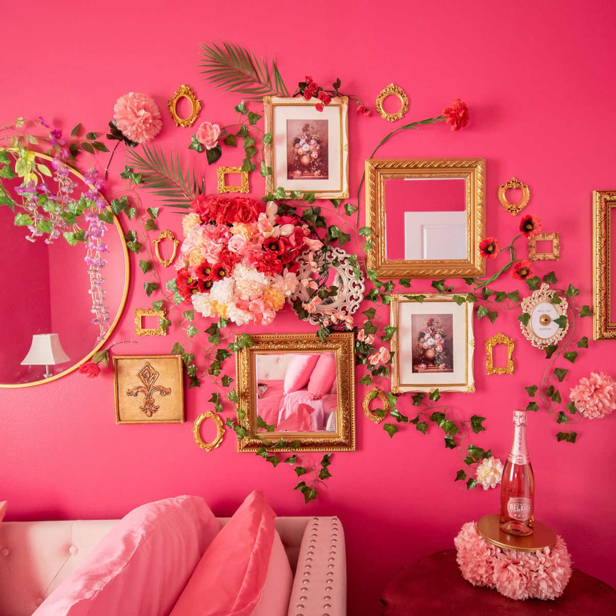 The scene features a vibrant pink wall adorned with floral decorations, framed photos, and a round mirror, alongside a sofa with pink pillows and a tabletop embellished with flowers and a bottle.