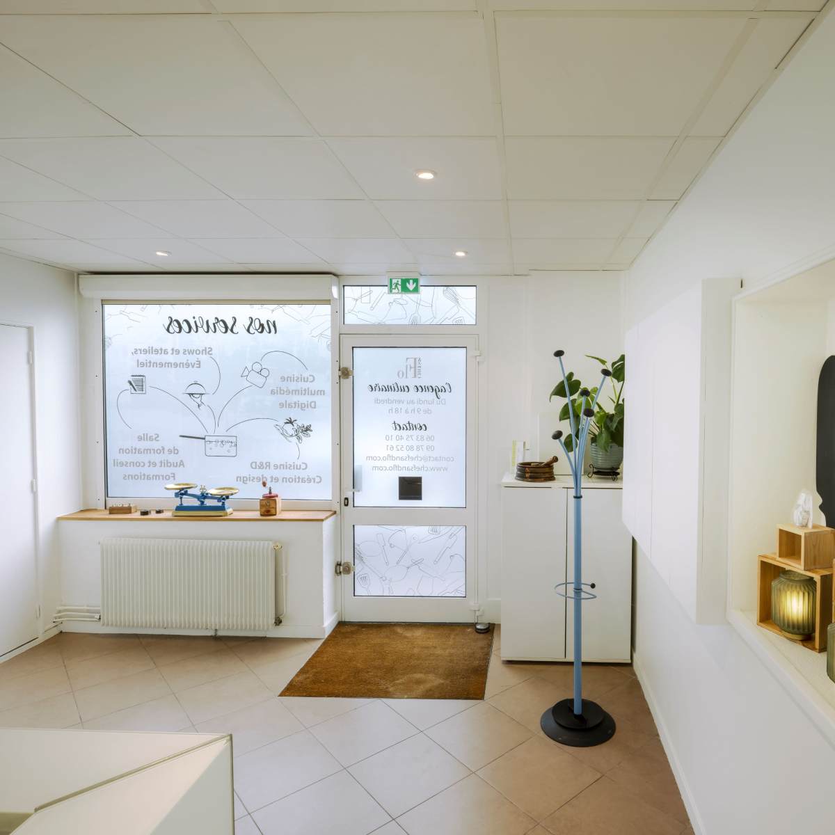 A bright, modern reception area with a large window, a mounted coat rack, and decorative plants on display.