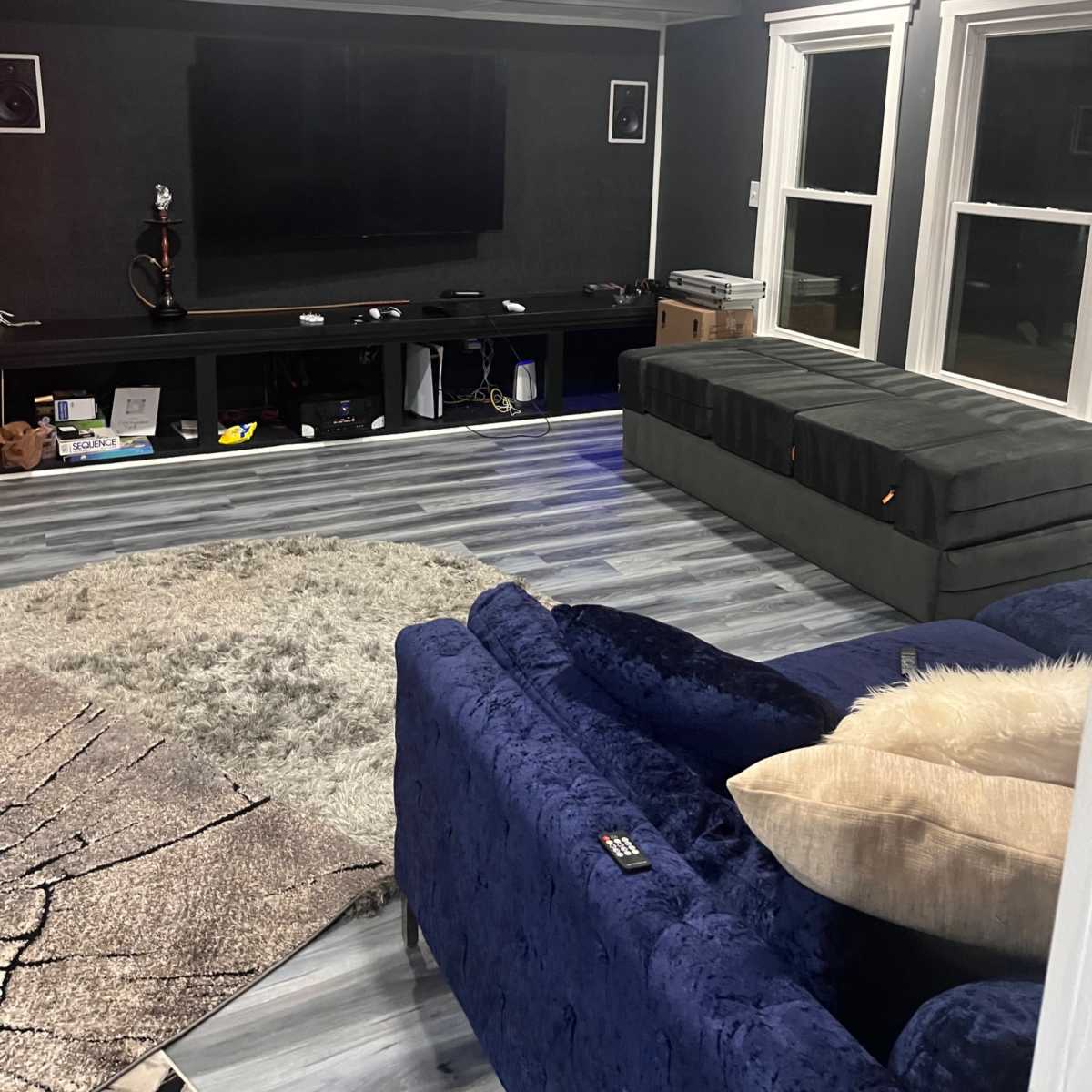 A modern living room with a dark gray wall, a television mounted on the wall, a green velvet sofa, and a gray area rug on the floor.