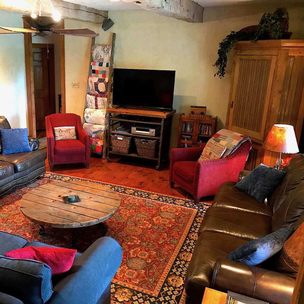 A rustic living room features a mix of leather sofas, upholstered chairs, a wooden coffee table, and a television surrounded by decorative furnishings.