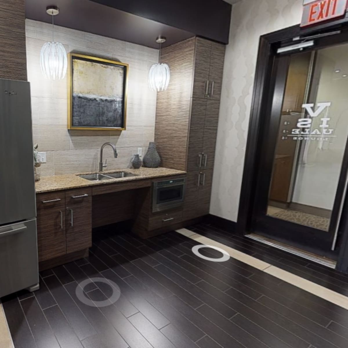 A modern kitchen corner with a stainless steel refrigerator, a sink, and cabinetry, featuring a piece of artwork on the wall.