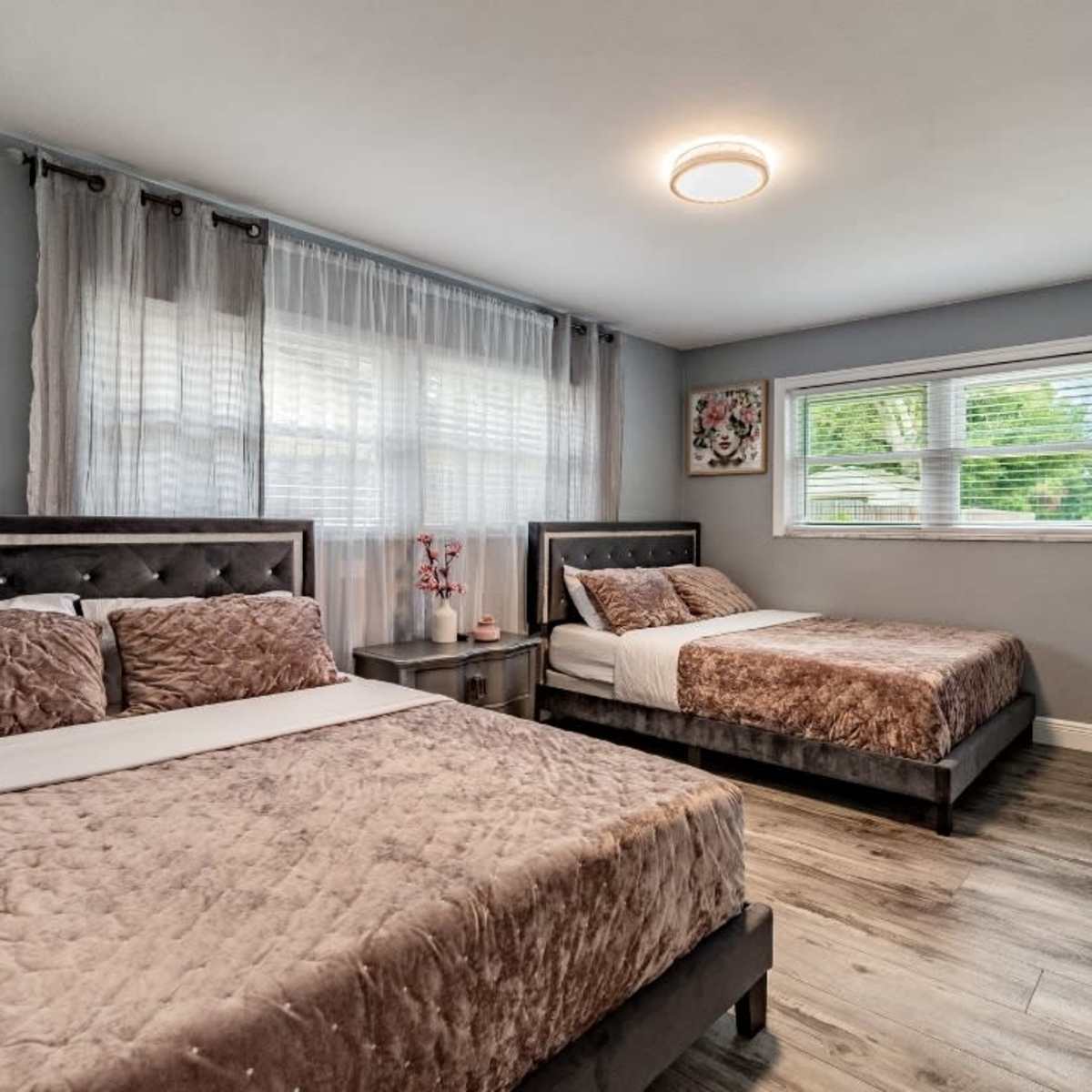 A bedroom featuring two beds with dark frames, a nightstand, and windows letting in natural light.