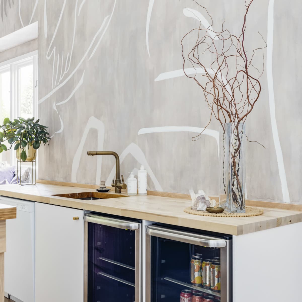 A modern kitchen with a wooden countertop, white cabinets, and a decorative vase with branches on the counter.