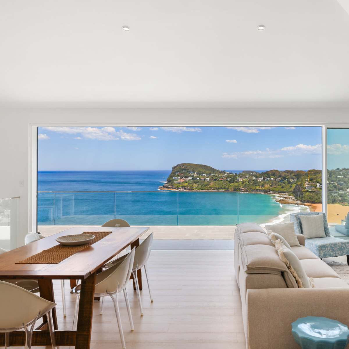 A modern living room features a large window showcasing a panoramic ocean view with a dining table and comfortable seating arranged inside.