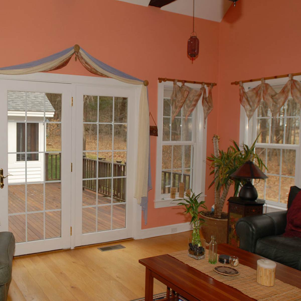 A cozy living room with a pair of French doors leading to a deck, flanked by windows draped with curtains.