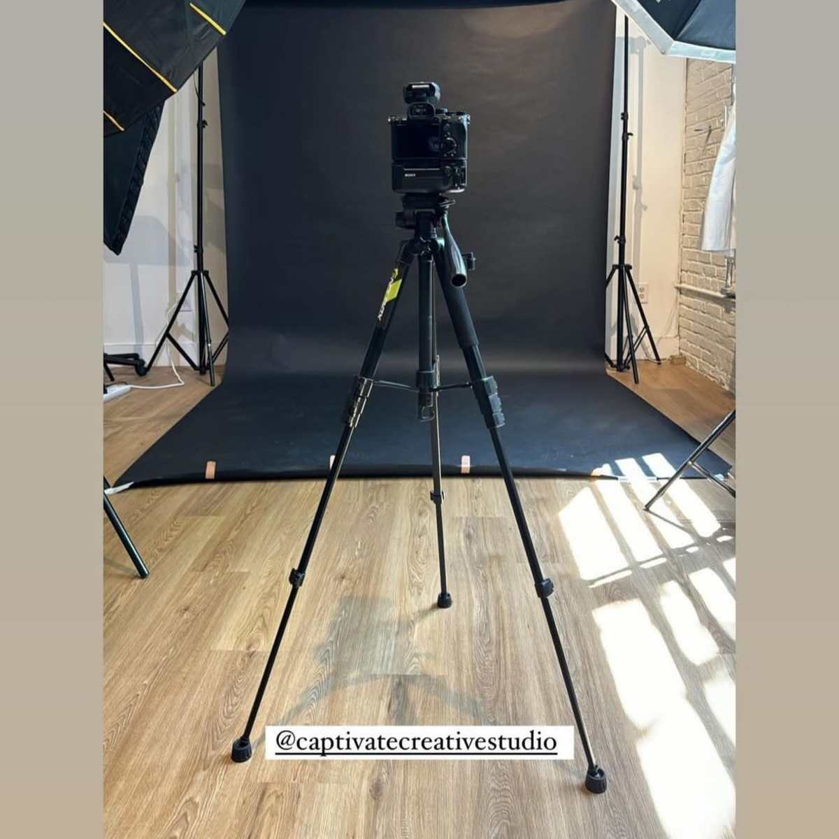 A camera on a tripod is placed in front of a black backdrop, surrounded by studio lighting equipment.
