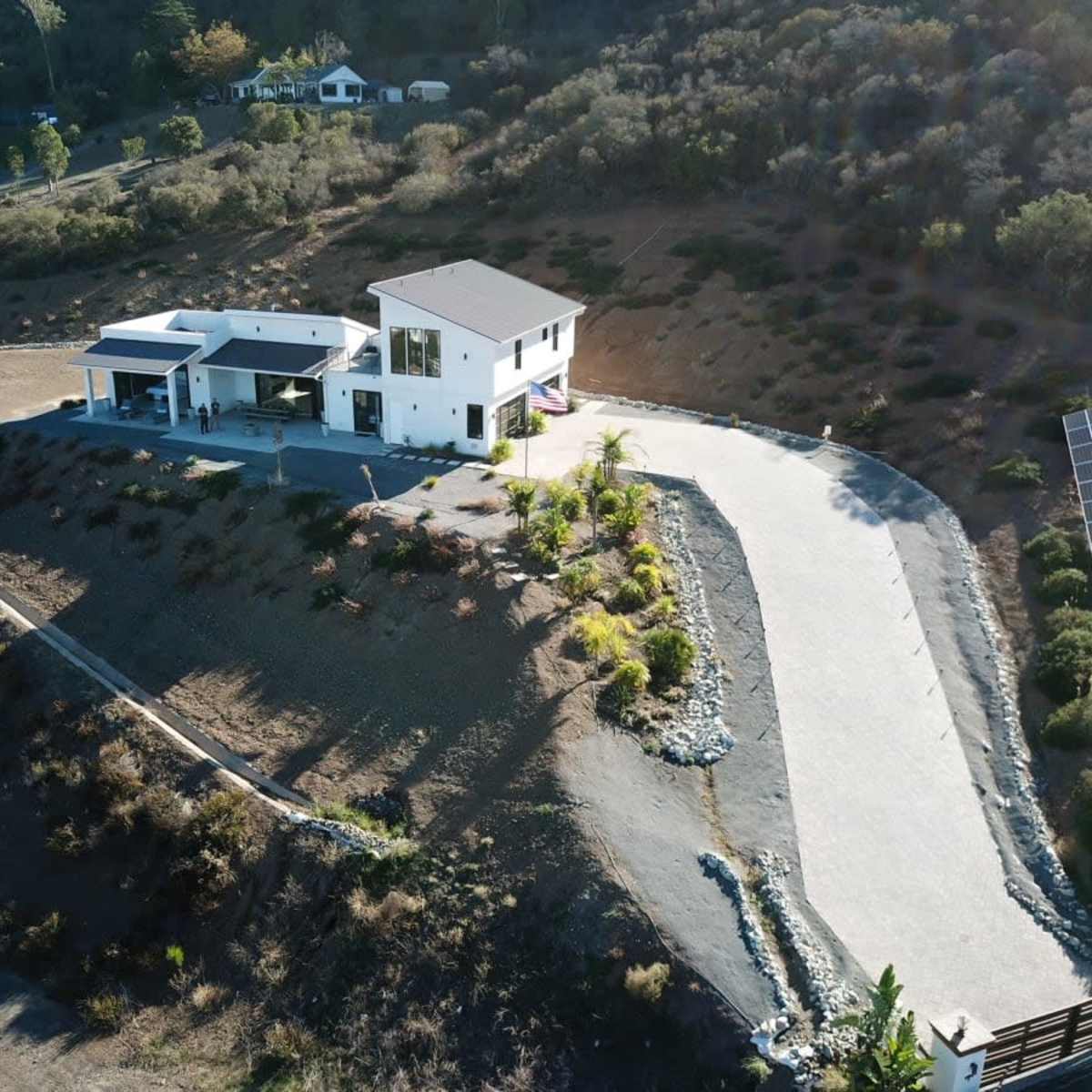 A modern two-story house situated on a hillside with a winding driveway and solar panels nearby.